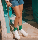 Woman wearing green glittery socks and white sneakers on a stone step with a colorful background